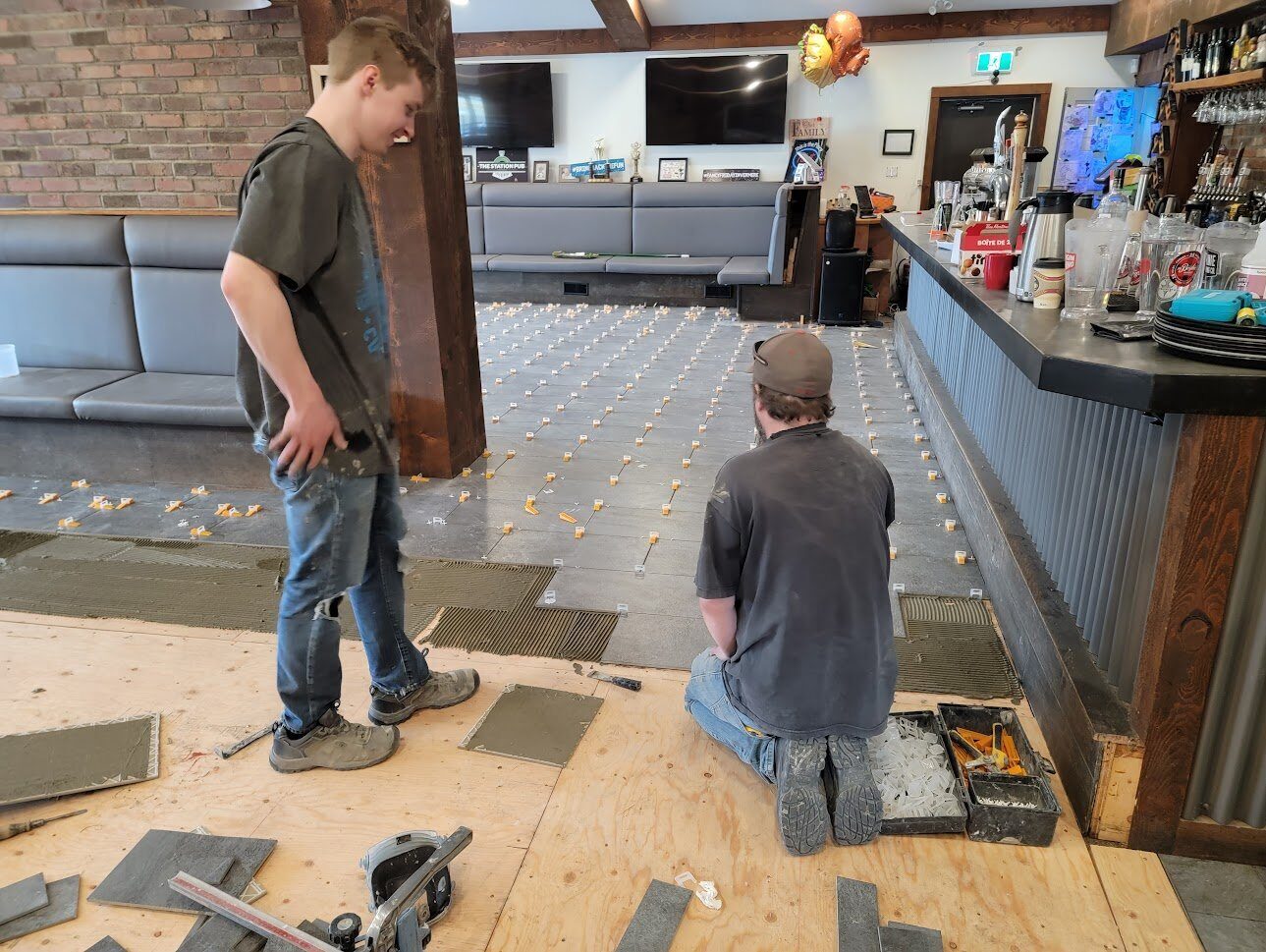Warwick Interiors team installing large-format tile flooring in a commercial bar and restaurant space, using spacers and leveling clips for a precise, professional finish.