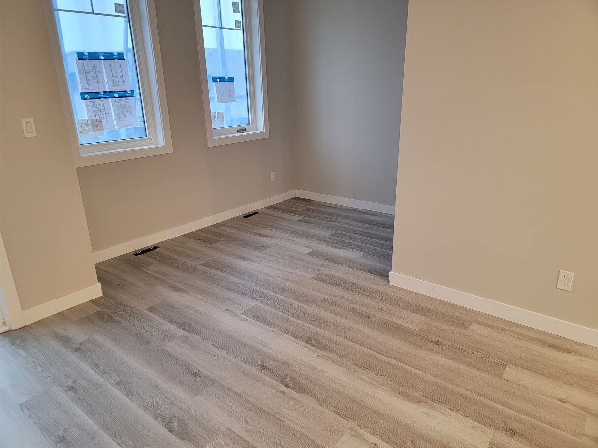 Warwick Interiors installed light grey luxury vinyl plank flooring in a bright room with neutral walls and natural light from two large windows."