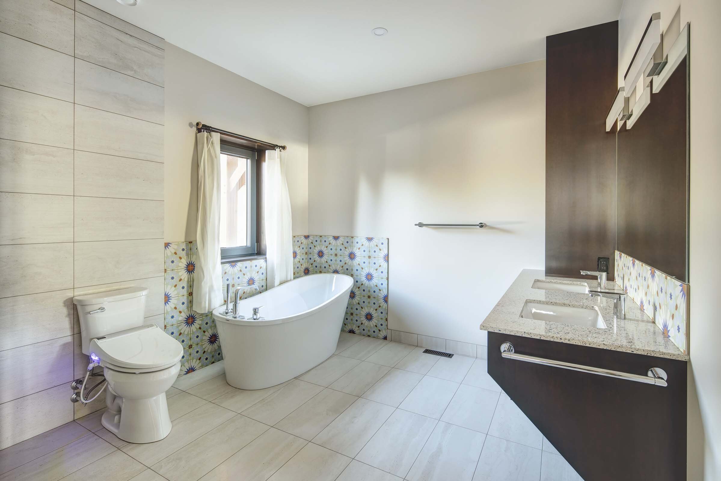 Modern bathroom by Warwick Interiors featuring freestanding tub, dual vanity with granite countertop, patterned tile backsplash, and large-format floor tiles.